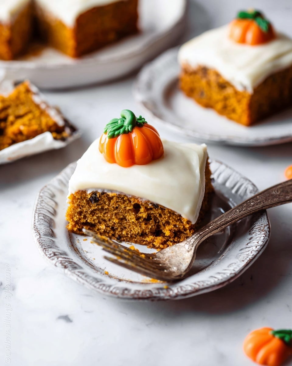 A piece of moist, orange-brown pumpkin cake with dark specks sits on a white plate with a vintage edge design. The cake has one thick layer topped with a smooth, thick layer of creamy white frosting. A small, bright orange pumpkin decoration with green leaves rests on top of the frosting. To the left, a woman's hand is holding a silver fork with a bite of cake and frosting on it. Another white plate with a similar cake piece and fork is slightly blurred in the background on a white marbled surface with pumpkin candy nearby. Photo taken with an iphone --ar 4:5 --v 7