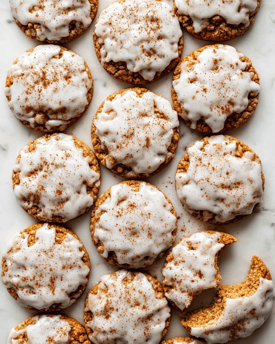 A group of fifteen round cookies arranged closely together on a white marbled surface, each cookie has a golden-brown base with a rough, textured look and is topped with a soft, uneven layer of white icing that drips slightly, sprinkled with a light dusting of brown cinnamon powder; one cookie in the lower right corner has a bite taken out, revealing the crumbly inside. photo taken with an iphone --ar 4:5 --v 7