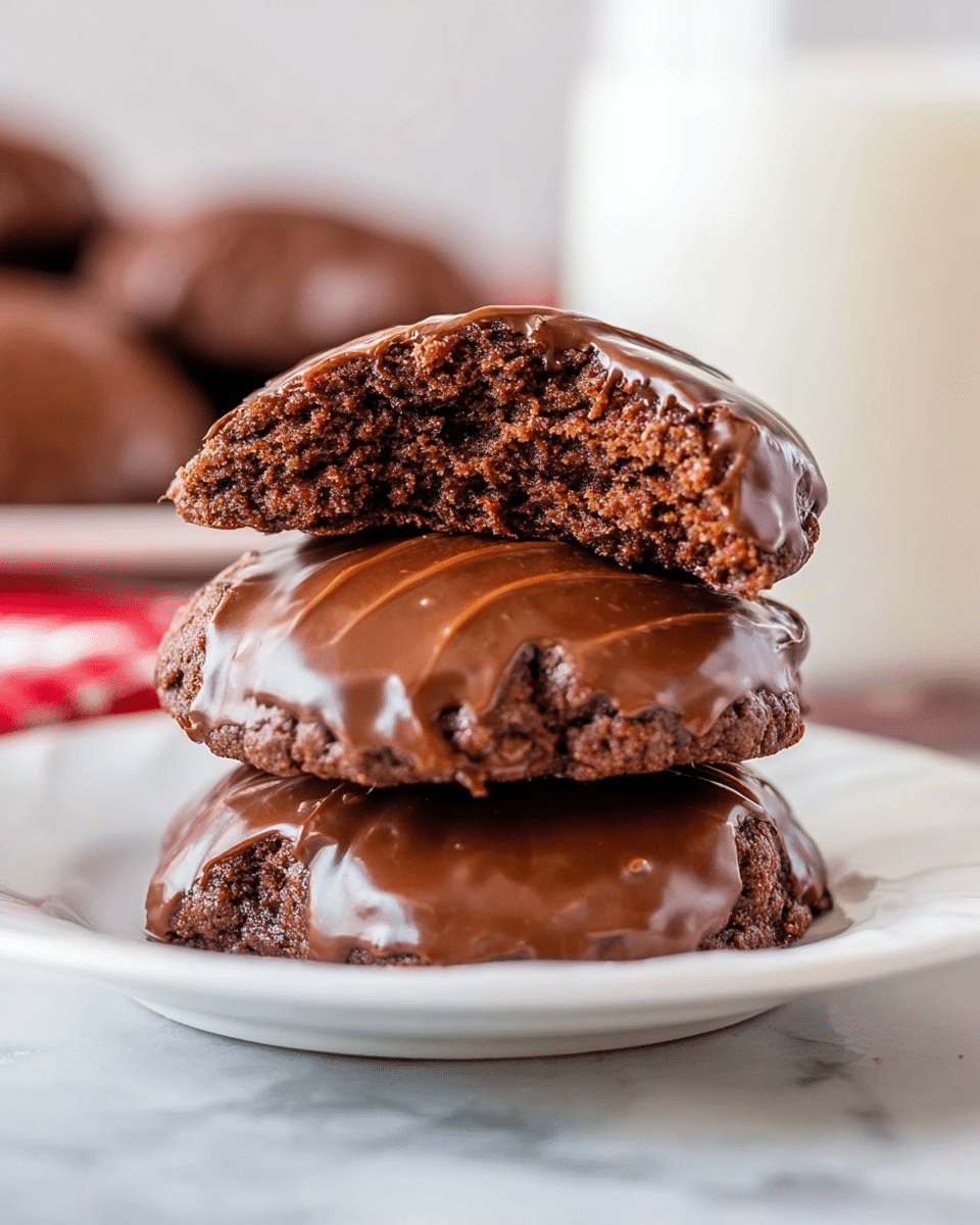 A stack of three soft chocolate cookies is placed on a white plate on a white marbled surface, with a glass of milk blurred in the background. The bottom two cookies are fully covered in smooth, glossy chocolate frosting with slight ridges and texture on the surface. The top cookie is cut in half and placed on top, showing a moist, dense chocolate interior with a slightly cracked texture. The cookies have a rich brown color with the frosting slightly darker and shiny. photo taken with an iphone --ar 4:5 --v 7