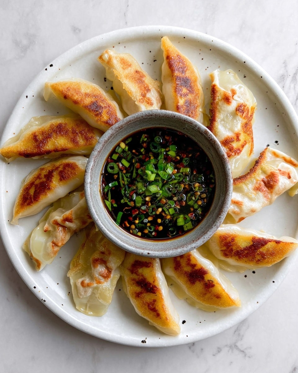 A white round plate holds seven golden-brown pan-fried dumplings arranged in a loose circle. Each dumpling has a slightly crispy, browned texture on one side, with translucent, soft dough on the other parts. In the center of the plate is a small, rustic gray bowl filled with a dark soy-based dipping sauce topped with bright green chopped scallions. The plate rests on a white marbled surface. photo taken with an iphone --ar 4:5 --v 7