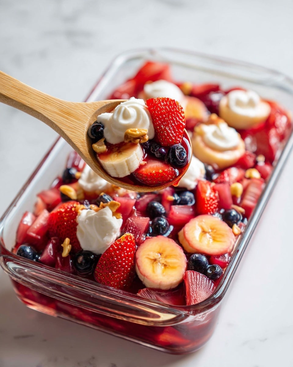 A close-up of a clear rectangular glass dish filled with a colorful fruit salad featuring several layers: the base consists of small chopped light pink and red fruit pieces, including strawberries and pineapple, mixed with dark purple blueberries; on top, a glossy, translucent red syrup coats the fruit, adding a shiny texture; scattered dollops of white whipped cream sit on the fruit surface, along with small orange-brown nut pieces; a wooden spoon is scooping the fruit from the bottom right corner. The dish is placed on a white marbled surface. Photo taken with an iphone --ar 4:5 --v 7